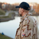 Man wearing a navy blue lightweight foldable tactical baseball cap with camouflage jacket by a riverbank