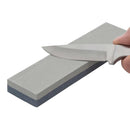 Double-sided vintage sharpening stone made of durable aluminum oxide with a knife blade being sharpened on top