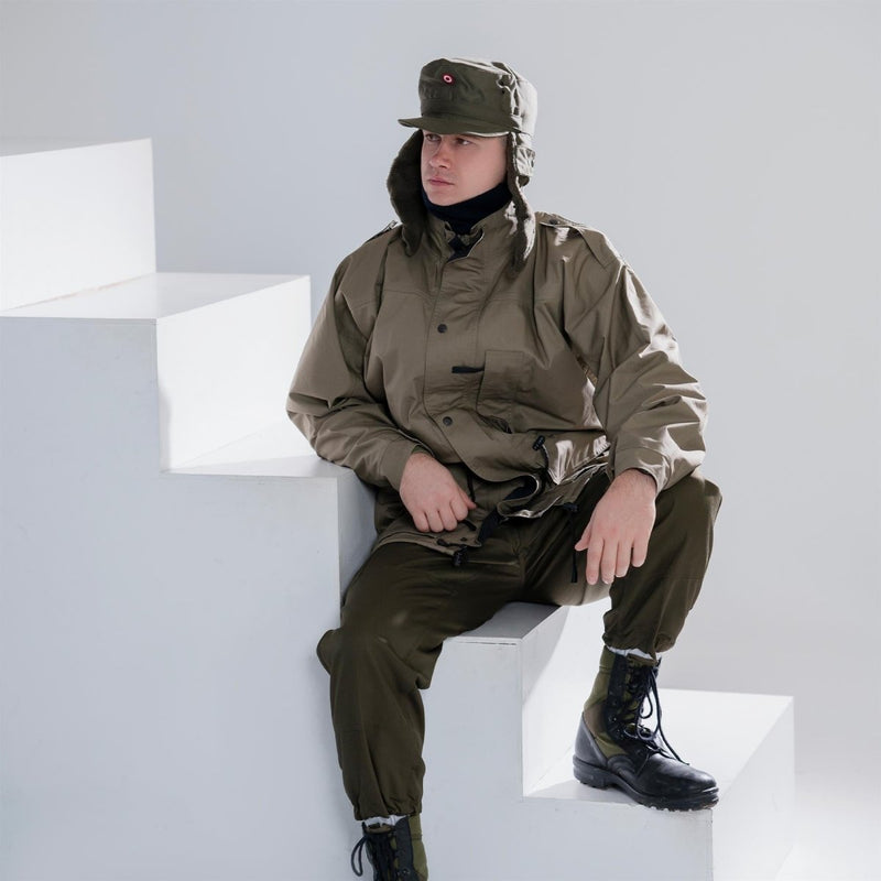 Man wearing genuine Austrian army olive winter cap with insignia and matching military outerwear sitting on white stairs