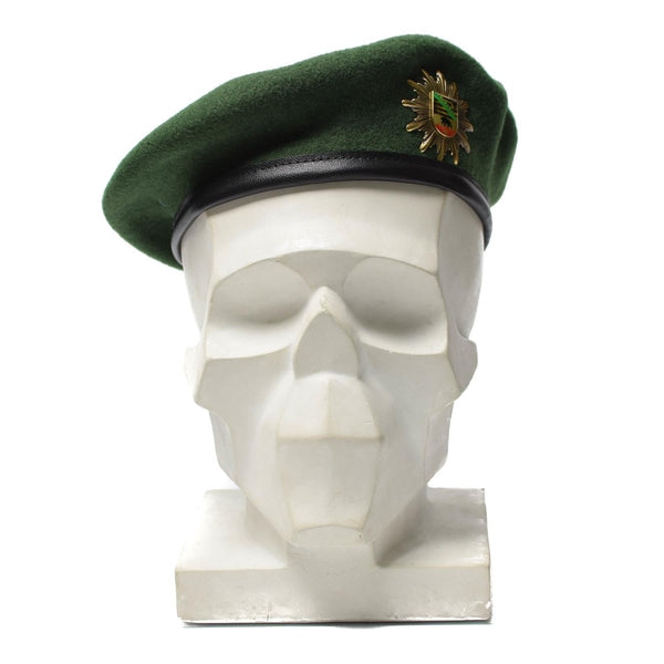 Green German police wool beret hat with metal cockade insignia displayed on white mannequin head