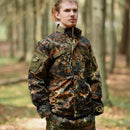 Man wearing MFH Brand U.S. Military style flecktarn camo ripstop jacket in forest setting with hands in pockets