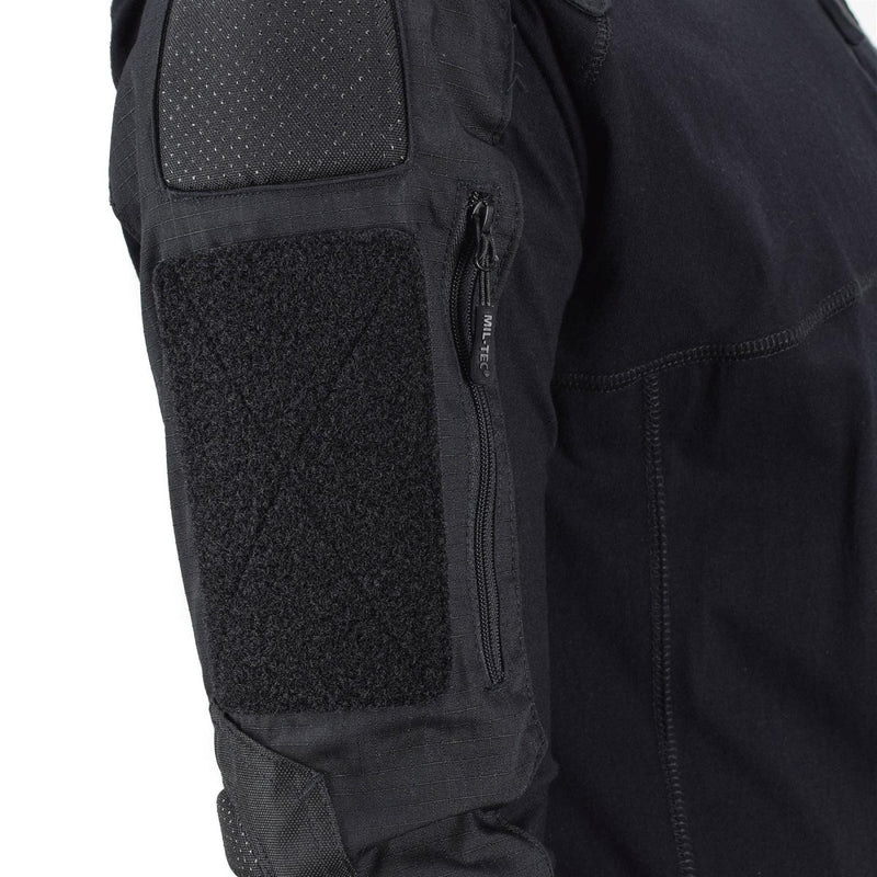 Close-up of black Mil-Tec tactical combat shirt sleeve with padding, zipper pocket, and durable stitching details.