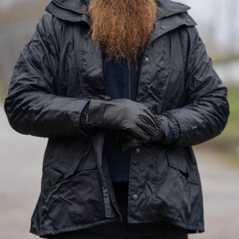 Person wearing black tactical leather gloves and a black jacket outdoors with a blurred background