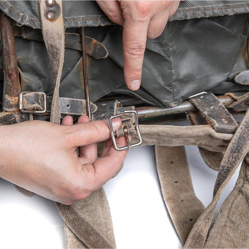Close-up of hands adjusting the leather harness buckle on a vintage Finnish military waterproof backpack.