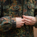 Close-up of hands adjusting zipper on Original German army field jacket parka with flecktarn camouflage pattern and hood