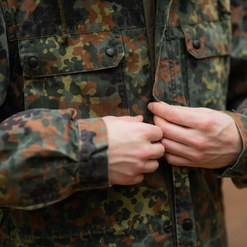 Close-up of hands adjusting zipper on Original German army field jacket parka with flecktarn camouflage pattern and hood