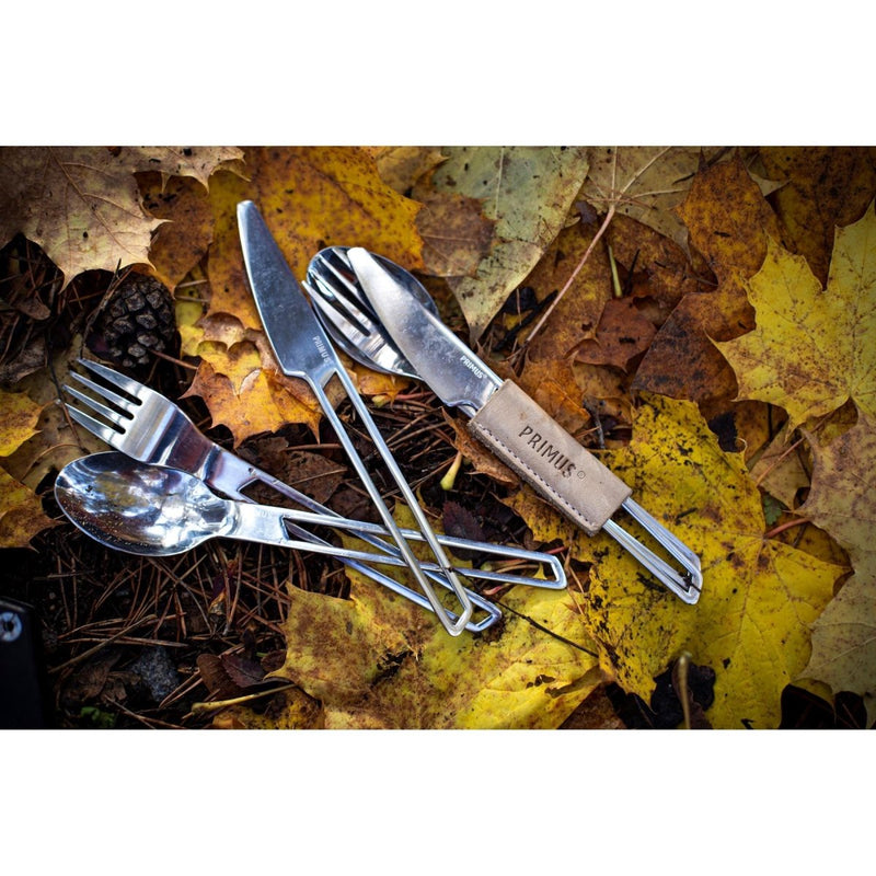 Lightweight stainless steel camping cutlery set with knife, fork, spoon, and leather sleeve on autumn leaves background.