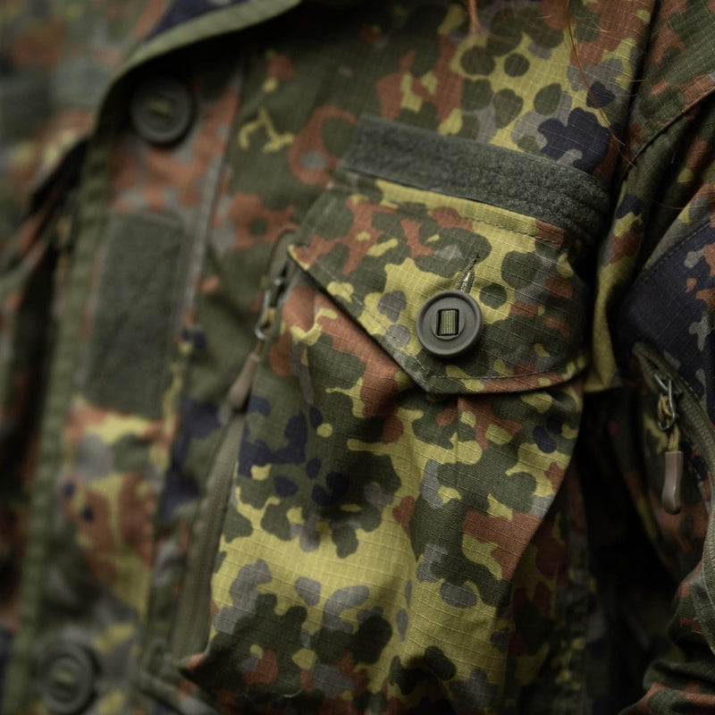 Close-up of TACGEAR Flecktarn camouflage tactical jacket pocket with button closure and durable ripstop fabric detail